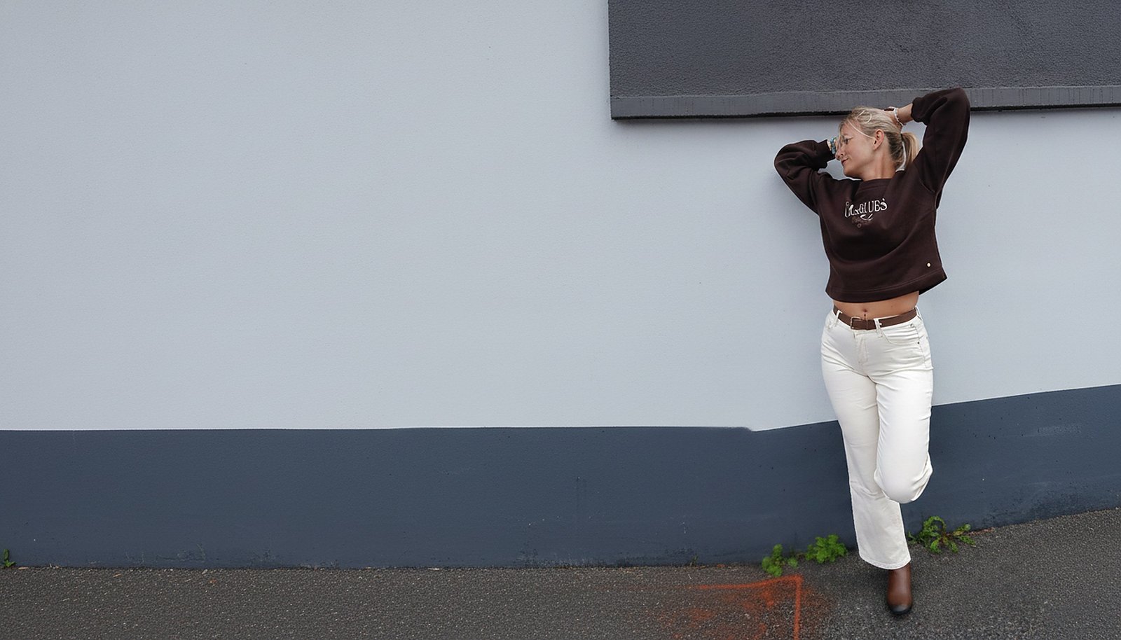 Laurie porte un sweat Red Button et un pantalon à ceinture marron devant un mur clair