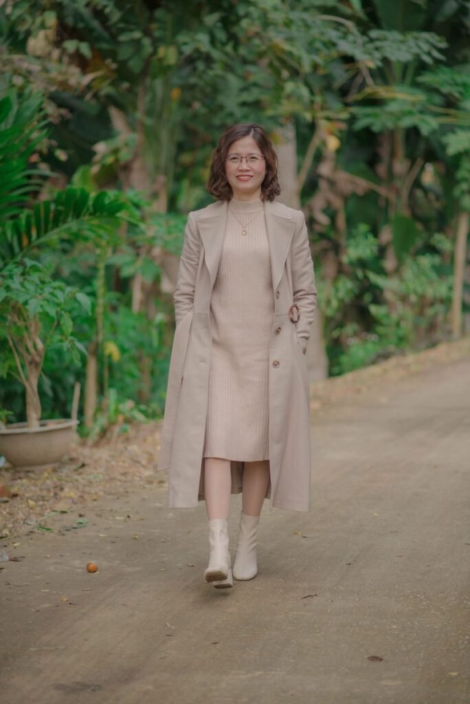 Femme en robe midi en maille beige sous un long manteau assorti, avec des bottines blanches