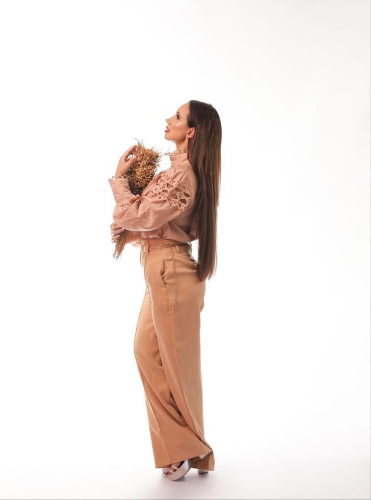 Femme en pantalon large camel et blouse rose poudré à manches brodées, de profil sur fond blanc