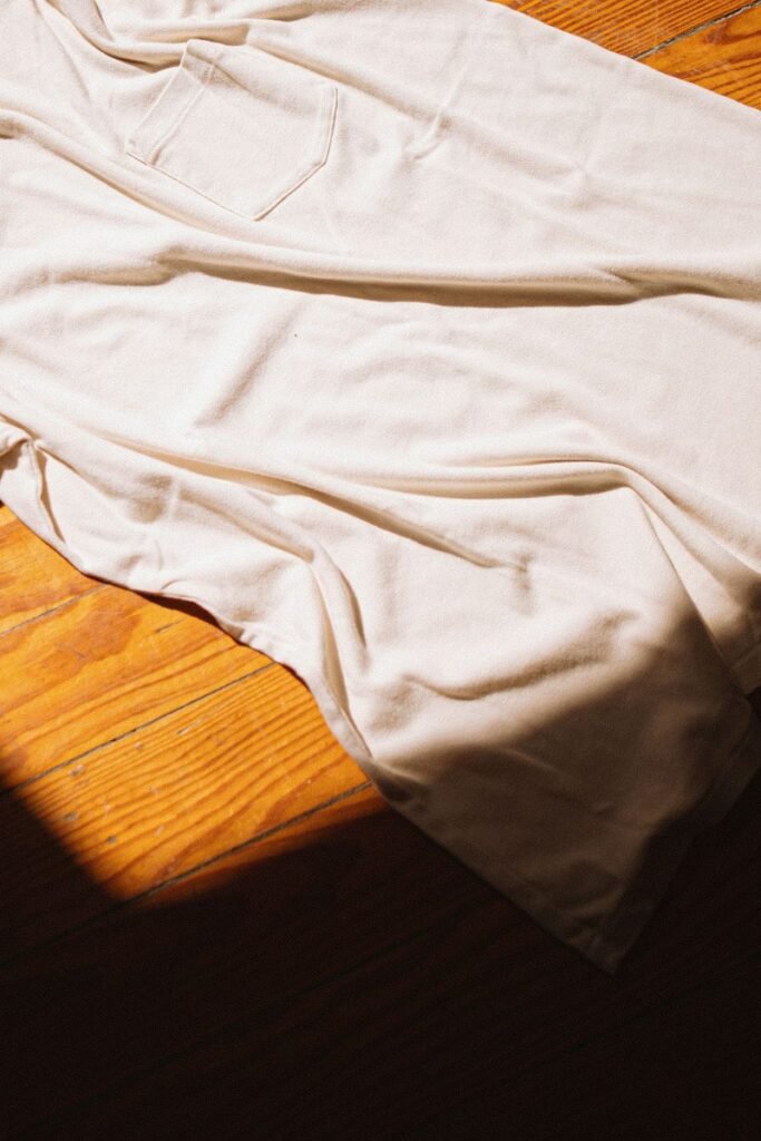 Tee-shirt en coton blanc à poche étalé sur un parquet, dans un rayon de soleil
