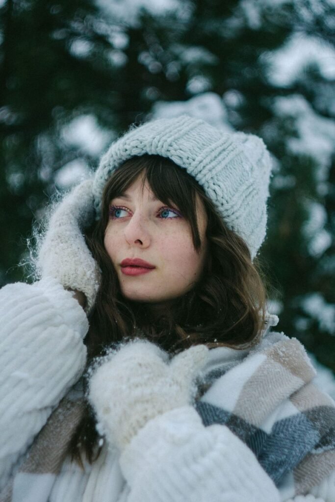 Femme en bonnet en grosse maille gris clair, moufles en laine et écharpe à carreaux sous la neige