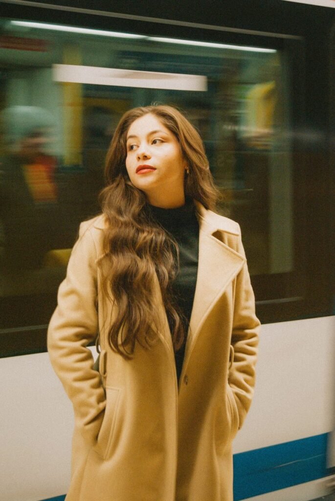 Femme en manteau camel ouvert sur un col roulé noir, sur un quai de métro devant une rame en mouvement